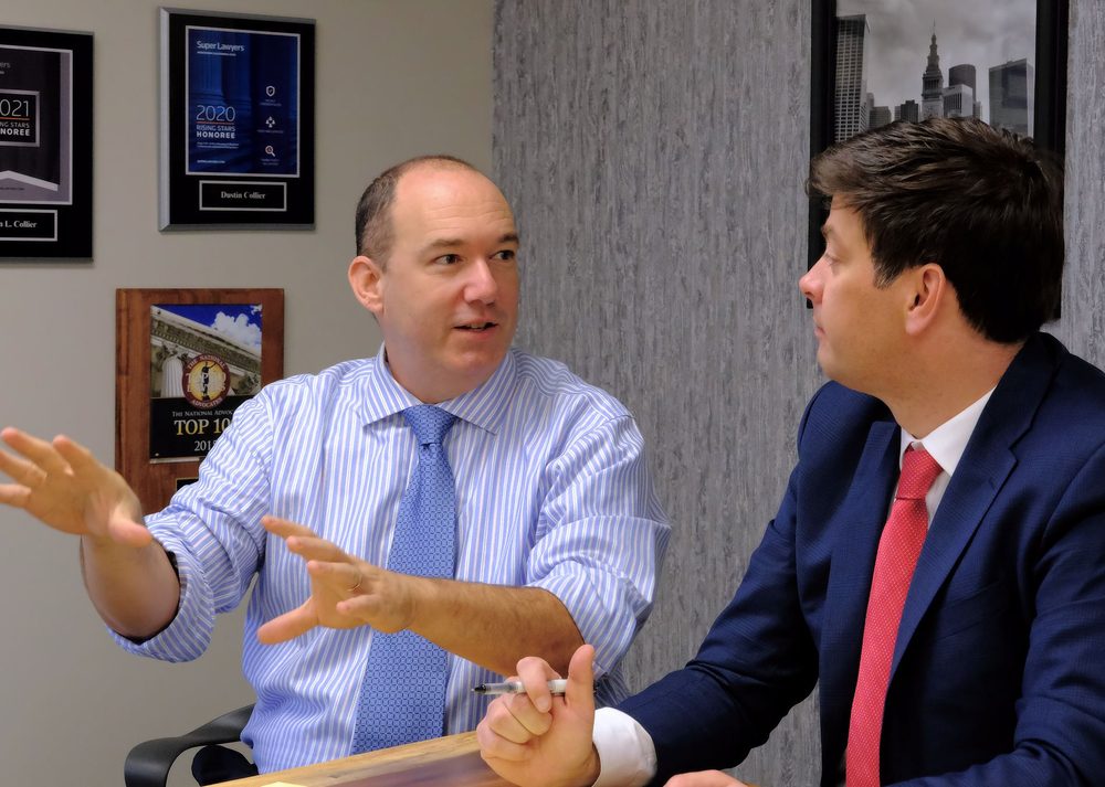 Drew Teti and Dustin Collier in discussion at a conference table, awards on the wall behind them